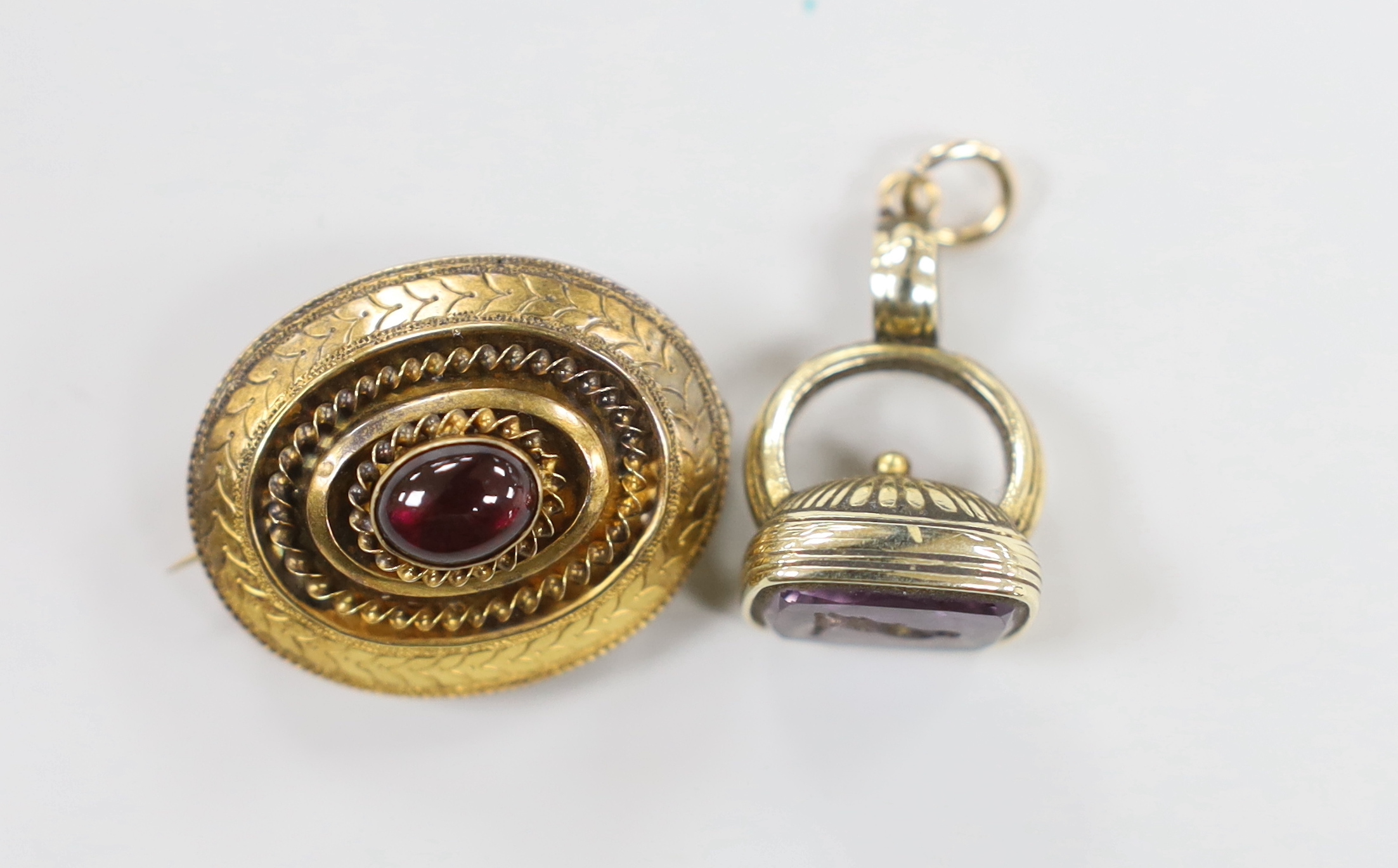 A Victorian yellow metal and single stone cabochon garnet set oval brooch, with glazed back, 29mm and a similar yellow metal overlaid and amethyst set fob seal, the matrix carved with a bird.
